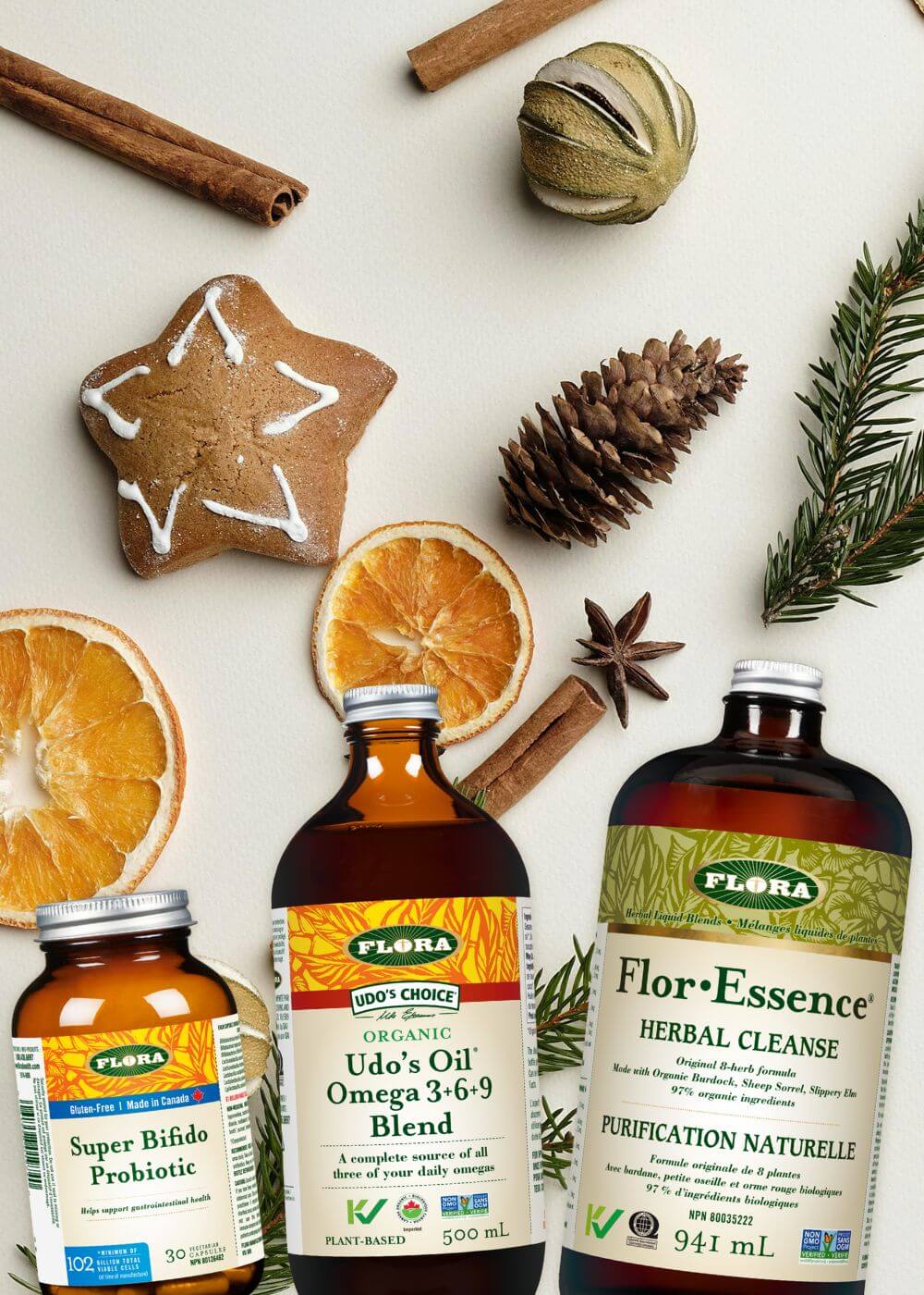 Four Flora supplement bottles on a white background with decorative elements like cinnamon sticks and oranges.