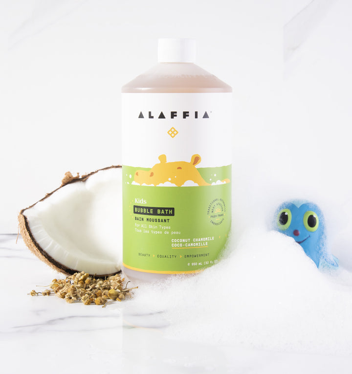 Fair trade kids' bubble bath by Alaffia with coconut and chamomile pictured with coconut, chamomile flowers, and bath toy