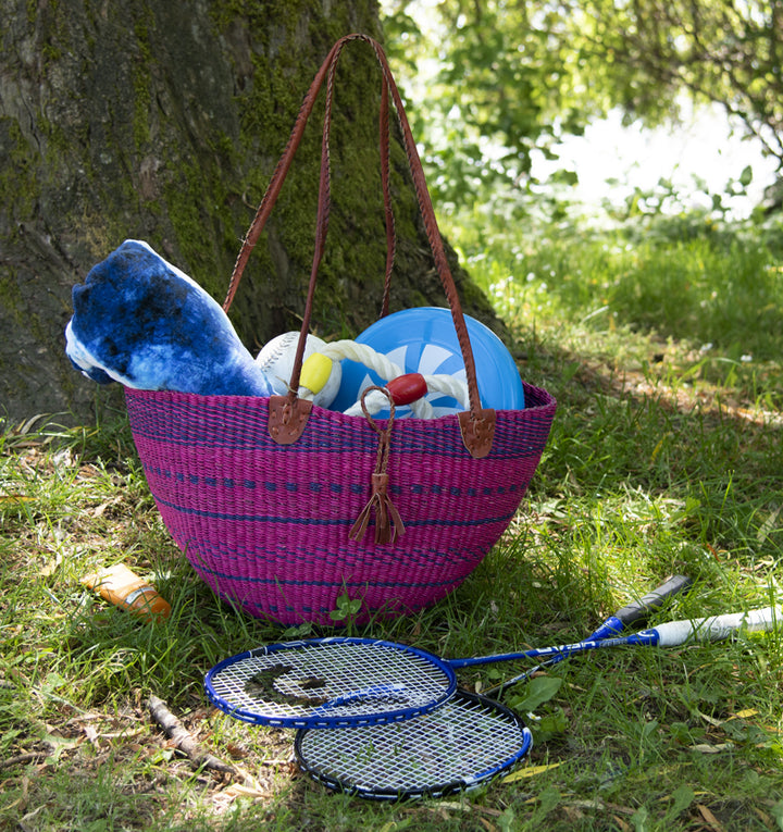 Purple hand woven basket, fair trade by Alaffia in Africa, filled with sports equipment at park